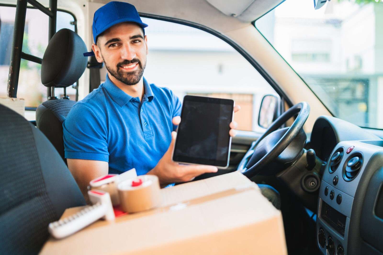 Portrait of a delivery man driver using digital tablet while sitting in van. Delivery service and shipping concept.