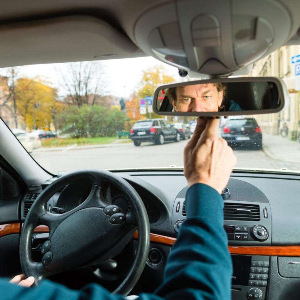 Experienced taxi driver is looking in the rear view mirror in his taxi, he sets the taximeter