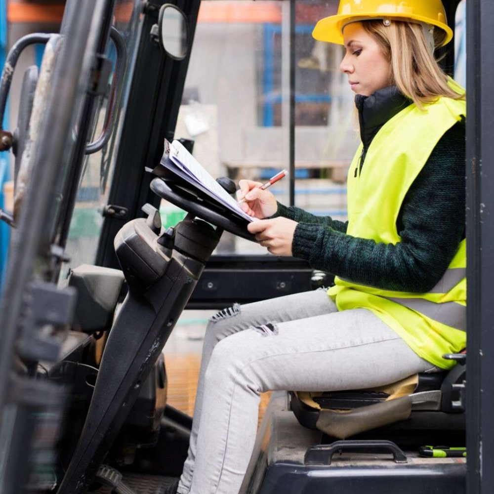 Female forklift truck driver outside a warehouse. A woman sitting in the fork lift making notes.