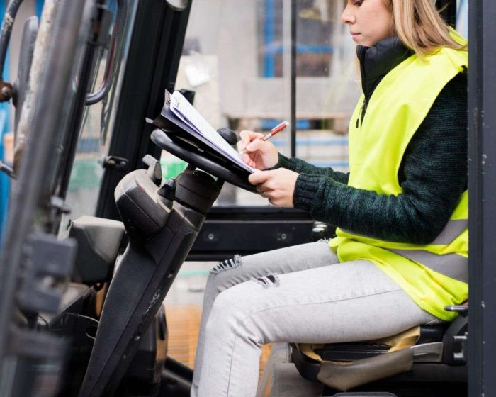 Female forklift truck driver outside a warehouse. A woman sitting in the fork lift making notes.